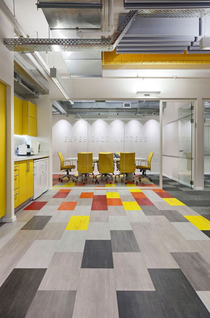 עיצוב חדר ישיבות להייטק סמוך למטבחון צהוב עם רצפת אריחים צבעונית ותקרה חשופה