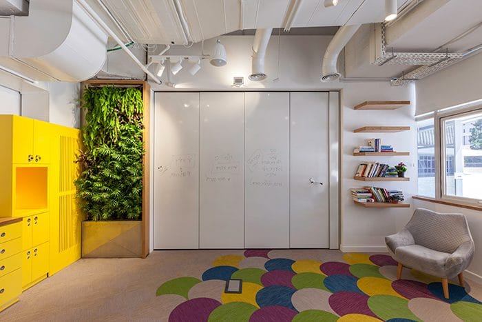 עיצוב מרכז חדשנות צבעוני עם שילוב קיר ירוק, רצפה בצבעי קשת, מטבחון צהוב ותקרה חשופה צבועה לבן